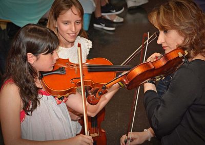 Niña y Profesora tocando el Violín. Otra niña las observa en segundo plano