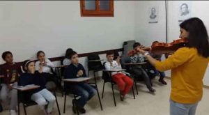 Niños en clase música observando profesora tocando violín