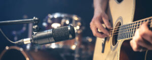Manos tocando la guitarra hacia un micrófono