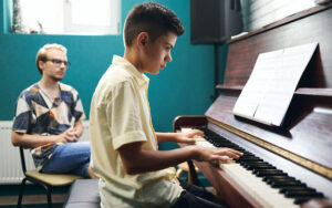Aula de música con niño tocando el piano bajo la supervisión del profesor