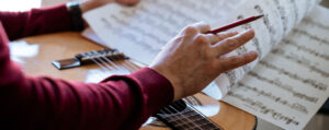 Manos de un adulto pasando páginas de partituras sobre una guitarra