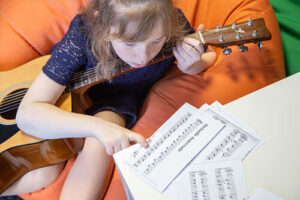 Chica joven leyendo partituras musicales con una guitarra