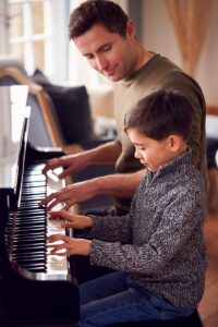 Niño muy pequeño tocando el piano junto a su profesor en clase de música.