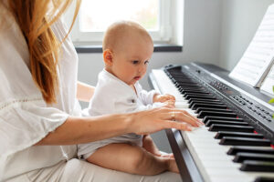 Bebé en el regazo de su madre, tocando las teclas de un piano en clases de estimulación musical.