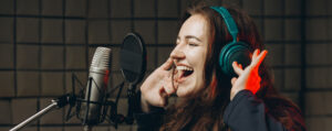 mujer joven cantando con cascos y expresión de felicidad frente a micrófono de estudio